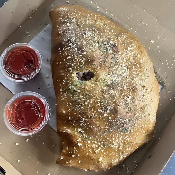 Al's Pizza calzone, dusted with parmesan, served in a box with two cups of marinara sauce.