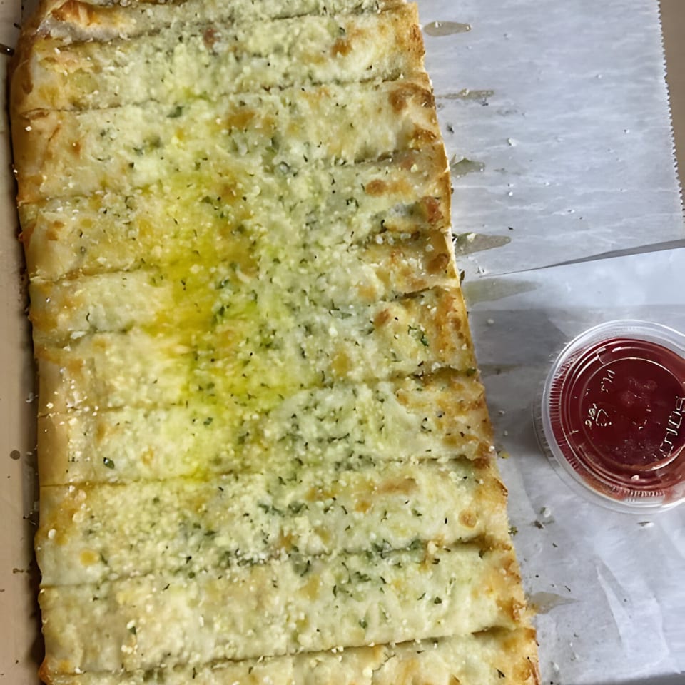 Al's Pizza garlic breadsticks, topped with cheese and herbs, with a side of marinara sauce.